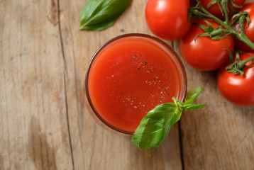 fresh tomato juice in a drinking glass with basil garnish on a rustic wooden board, healthy...