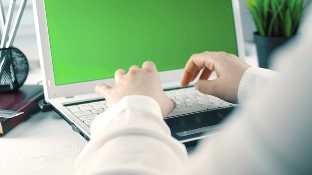 Young girl working on laptop with green screen in office. Close up 4k footage.
