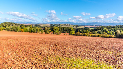 Typical red soil of countryside around Nova Paka. Agricultural Landscape with Giant Mountains on the background. Czech Republic. - obrazy, fototapety, plakaty