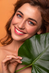 Naklejka premium Cute ordinary young woman posing with monstera tropical leafs. Fresh clean skin with flawless texture. Skin care beauty cosmetology concept. Space for text