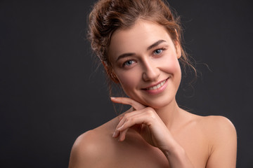 Fototapeta premium Cute smiling brunette caucasian woman posing on grey background. Fresh, clean, healthy, flawless skin. Space for text.