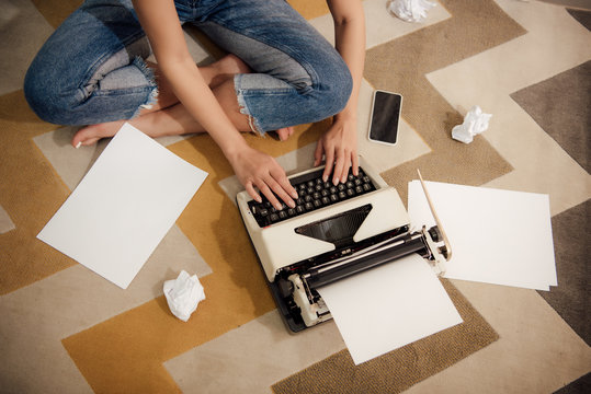 cropped shot of young barefoot woman sitting on floor and using typing machine