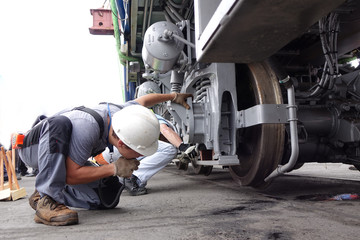 An engineer radios a crane operator to guide a suspended railway engine onto the tracks by placing the wheels
