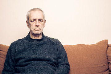 Dramatic portrait of a sad and depressed adult man sit on a sofa and  looking into space with...