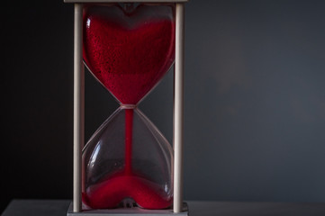 Hourglass as love concept for valentines day on dark gray background. The sand is running out. With...
