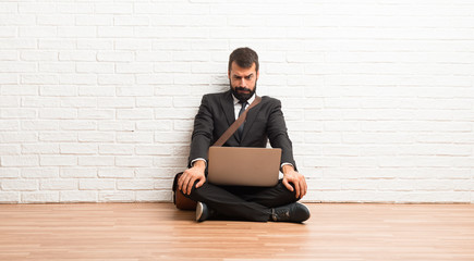 Businessman with his laptop sitting on the floor is a little bit nervous and scared pressing the teeth