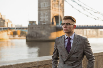 Portrait of the elegant young man who is standing outdoor against the background of river and bridge