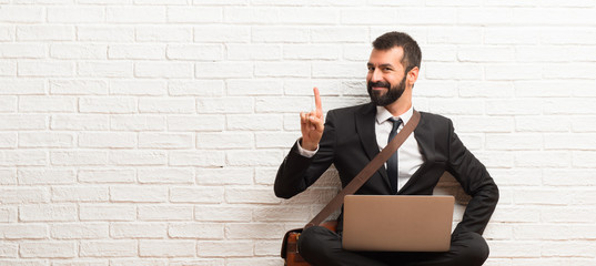 Businessman with his laptop sitting on the floor showing and lifting a finger in sign of the best