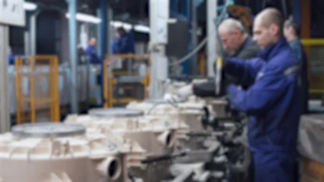 Blurred view of conveyor, master at work, part assembly process of element washing machine, assembly shop.