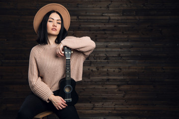 Portrait of a smiling casual woman posing with guitar against wooden plank