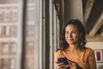 Smiling woman with smartphone looking through window