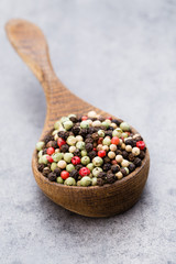 Peppercorn mix in a wooden bowl on grey table.