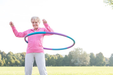 Senior woman doing gymnastic with hula hoop in park - obrazy, fototapety, plakaty