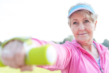 Determined senior woman exercising with dumbbell in park