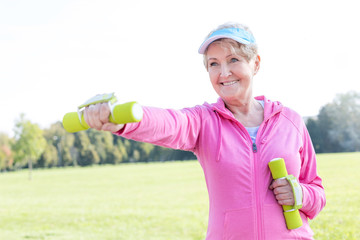 Dedicated senior woman exercising with weights in park