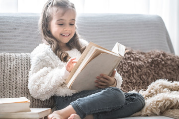 little girl reading a book on a comfortable sofa, beautiful emotions