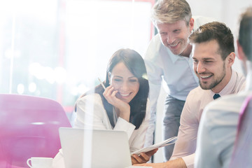 Smiling business people working on laptop at boardroom in office