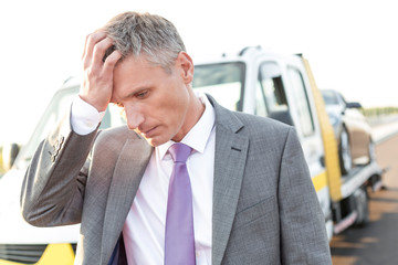 Tensed businessman standing against tow truck on road