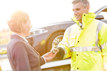 Smiling tow truck driver giving car key to businesswoman