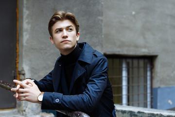 portrait of a man, on the street, in a suit and with a coat. it is worth leaning on the railing, on the steps. businessman. watch is on hand