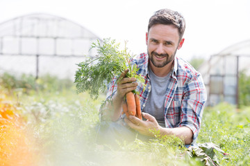 Portrait of smiling mid adult farmer harvesting carrots at farm