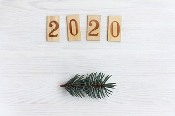 wooden figures denoting the year and spruce twigs on light wood surface top view / modest 2020