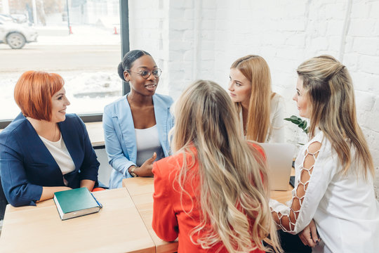 Team Work Process. Multiracial Group Of Young Women Collaborating In Open Space Office. Red-haired Mentor Coach Speaking To Young People, Teaching Audience At Training Seminar.