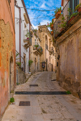Fototapeta na wymiar Italian narrow street with flower balconies in ancient baroque town Ragusa, Sicily, Italy