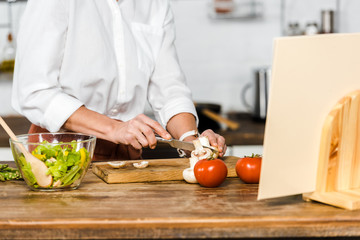 cropped image of mature woman cutting mushrooms in kitchen