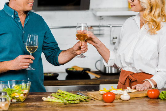 cropped image of mature husband giving glass of wine to wife in kitchen