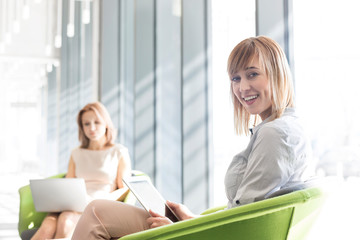 Smiling businesswoman using digital tablet with colleague in background at office