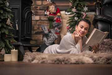Obraz na płótnie Canvas girl reading a book in a cozy home atmosphere near the fireplace