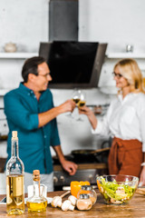 selective focus of mature wife and husband clinking with glasses of wine in kitchen