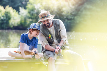 Happy father and son fishing in lake while sitting on pier