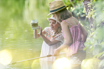 Smiling girl showing jar to friend while standing in lake
