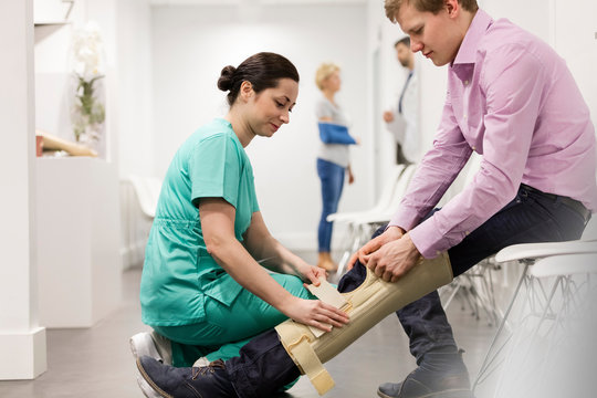 Nurse Assisting Patient In Wearing Knee Brace At Hospital