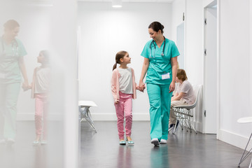 Smiling nurse walking with girl in corridor at hospital - obrazy, fototapety, plakaty