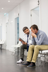 Doctor and mature patient over digital tablet in corridor at hospital