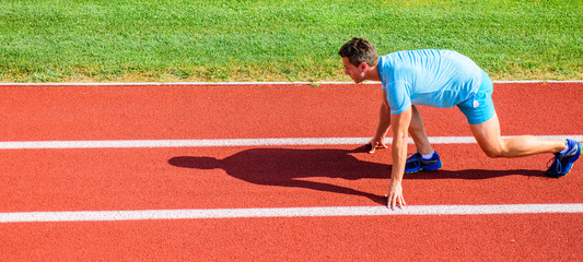 Sport motivation concept. Man athlete runner stand low start position stadium path sunny day....