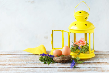 Easter concept. Bright spring flowers with Easter eggs near a yellow decorative lantern