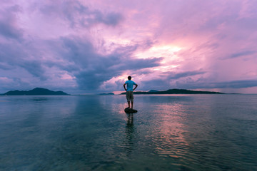 Alone man tourist standing on the stone in tropical sea and enjoying scenery during sunrise or sunset beautiful light dramatic sky environment in phuket thailand - obrazy, fototapety, plakaty