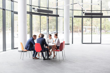 Business colleagues discussing while sitting at table during meeting in office lobby