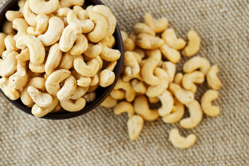 Cashew nuts in a wooden bowl on a burlap cloth background.