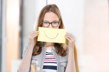 Creative businesswoman holding paper with smile drawn on it