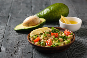 Clay bowl with amaranth salad and avocado fruit on a dark wooden table.
