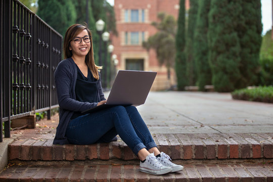 Solo Asian American Student On Laptop Computer Outside Residential Apartment Building Working Remotely