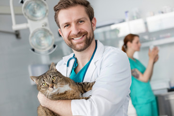 Portrait of smiling doctor carrying cat while standing at veterinary clinic