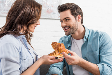 beautiful couple looking at each other and eating croissants during breakfast at home