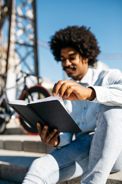 Mid adult man with bicycle sitting on stairs, reading in a book