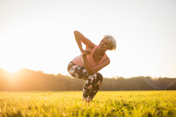 Senior woman doing yoga on rural meadow at sunset